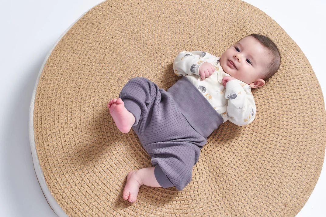 Baby mit langer Hose liegt auf einem Teppich Baby mit einem Luftballon in der Hand