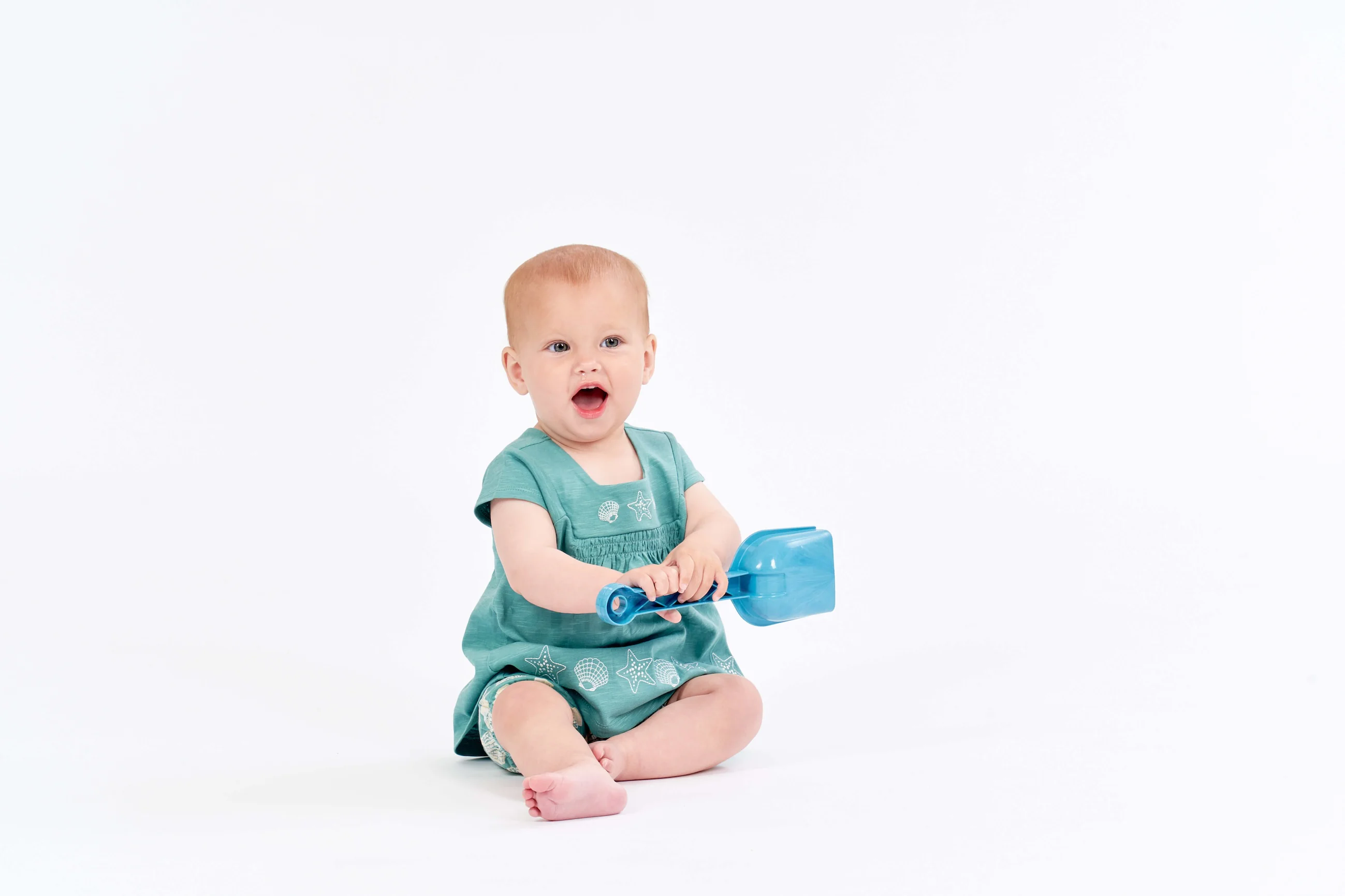Baby mit Kleid und Sandschaufel in der Hand