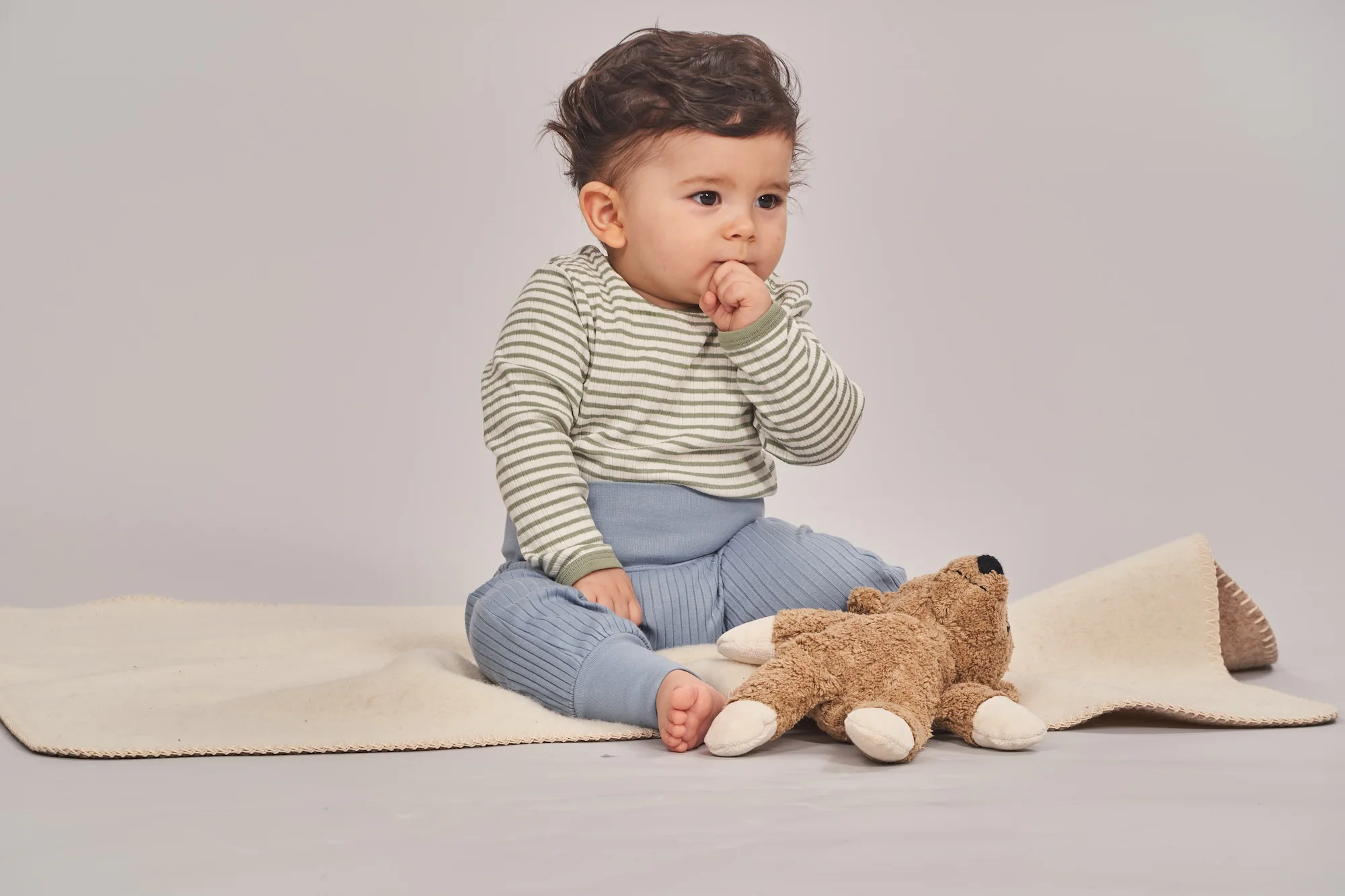 Baby sitzt auf einer Decke mit einem Kuscheltier