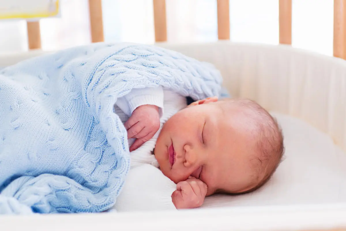 Baby im Bett mit blauer Decke