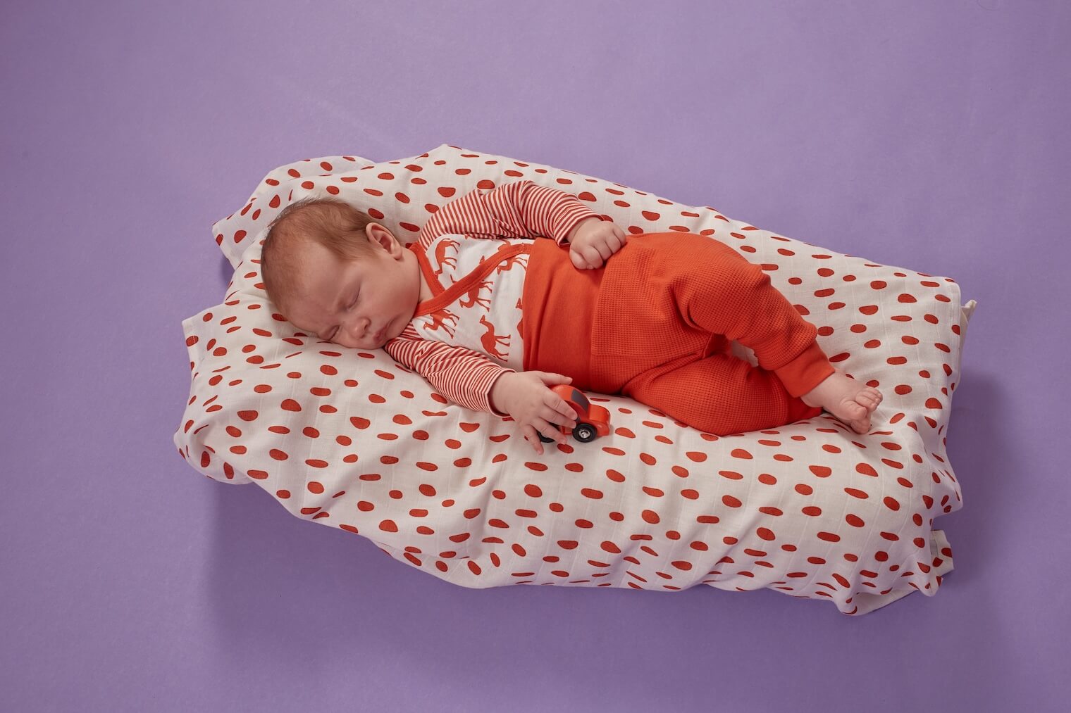 Baby mit Spielzeugauto liegt auf weichem Bett und schläft
