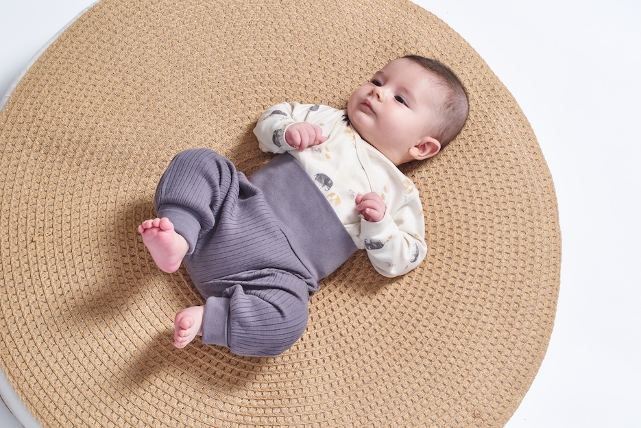 Baby liegt mit Wickelbody und Hose auf einem Teppich