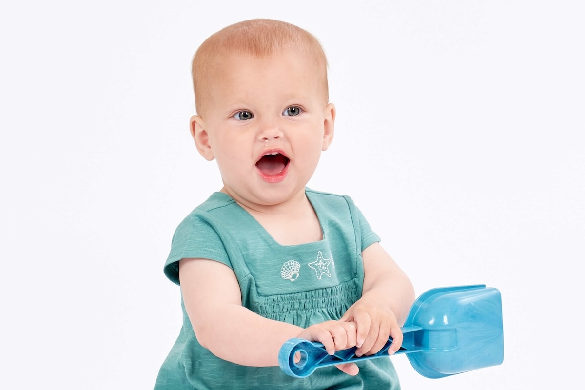 Baby im Kleid mit Sandschaufel