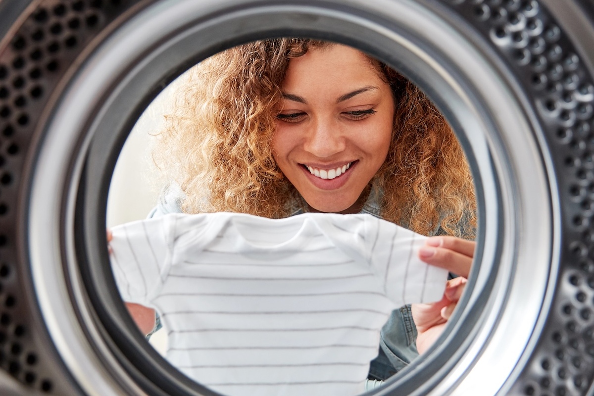 Eine Frau h&auml;lt einen Babybody vor der Waschmaschine